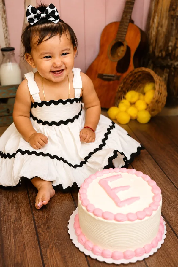 One year old smiling beside her first birthday cake