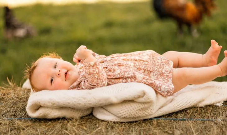 Baby on a knit blanket in the grass with the chickens