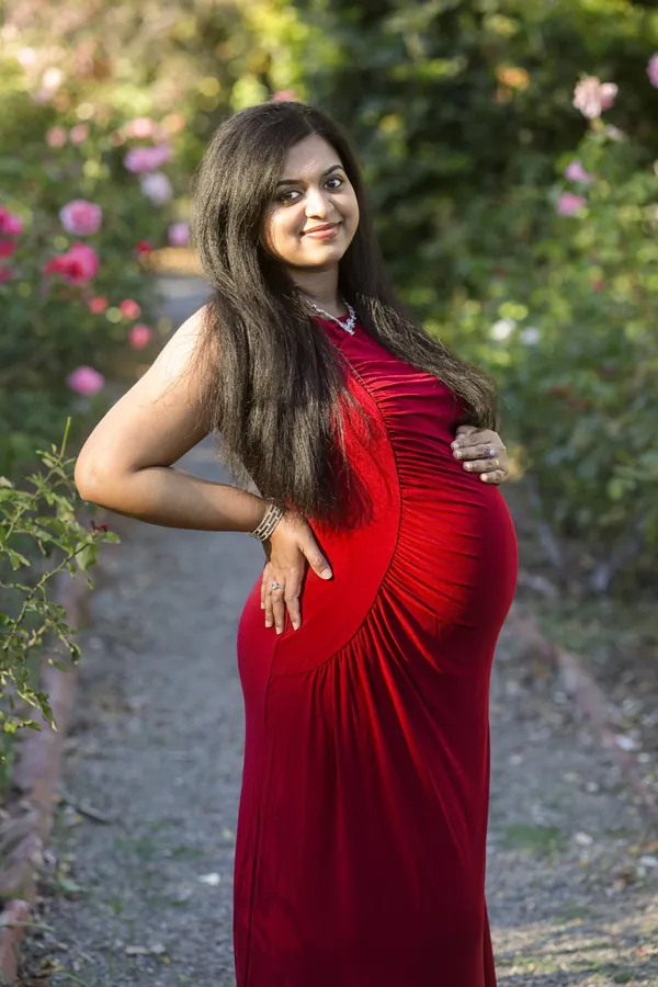 Maternity portrait in a deep red gown among the garden roses