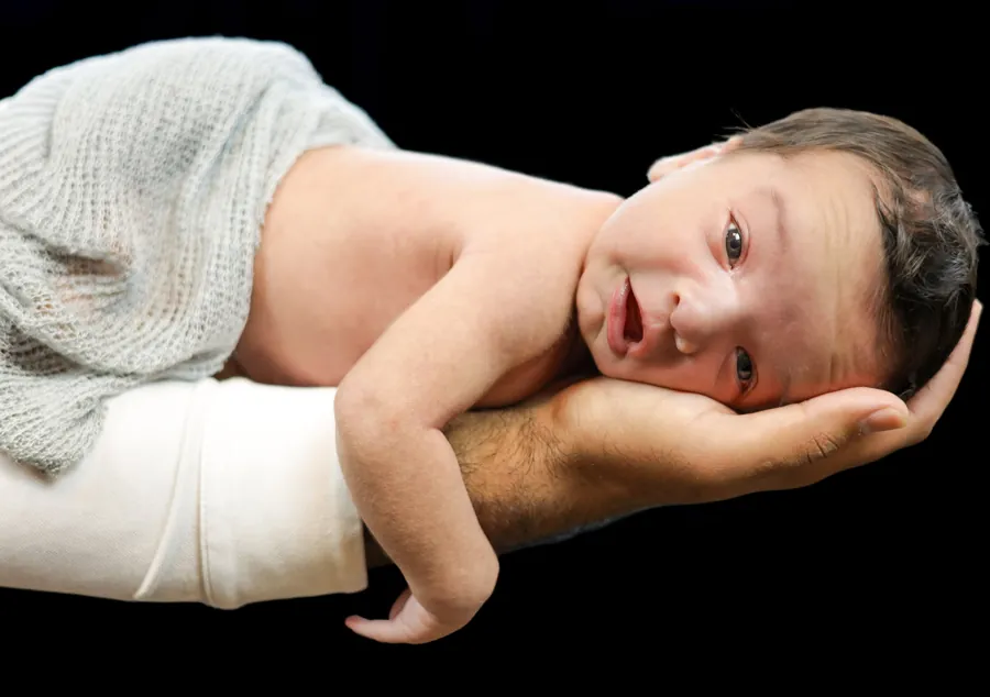 Newborn resting along a parent's forearm, head cupped in their hand, under a soft knit wrap