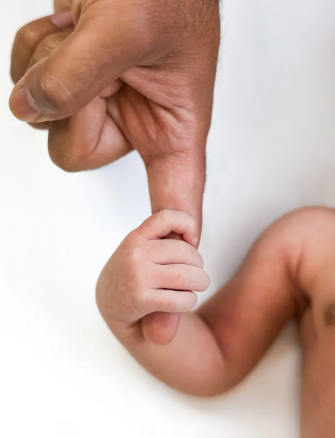 Newborn's tiny hand wrapped around a parent's thumb